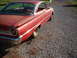 1961 Ford Starliner - Faded red 1960s coupe with chrome trim and round taillights sits on a gravel surface.