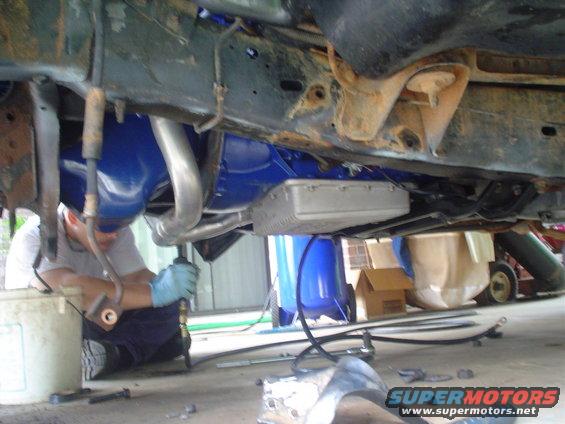 Undercarriage of a vehicle with blue painted components and exhaust pipes, a person works below