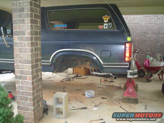 Dark blue Ford Bronco with rear axle raised on jack stands, tools scattered around