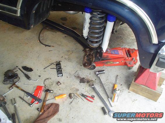 Blue vehicle's front suspension with new shocks and springs, jack, and tools on the floor