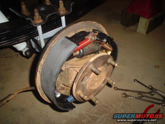 Vehicle brake drum assembly with brake shoes, springs, and wheel studs. Wrench set on floor