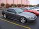2002 Ford Mustang - A gray 2002 Ford Mustang GT is parked in a lot with other vehicles.