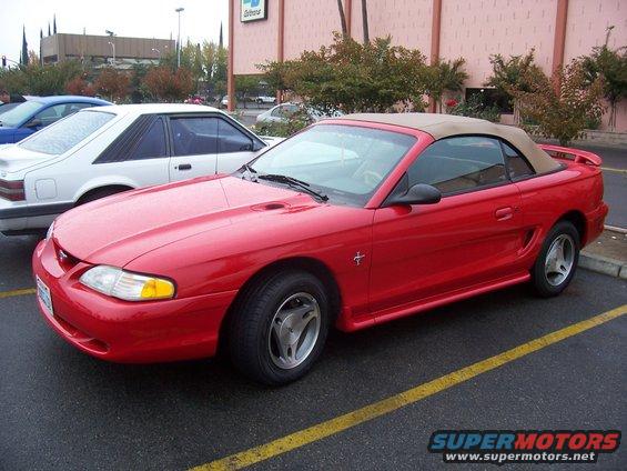 Red convertible Mustang parked next to a white coupe, front quarter view