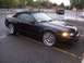2002 Ford Mustang - A black 2002 Ford Mustang convertible with custom chrome wheels is parked in a lot, with a pickup truck in the background.