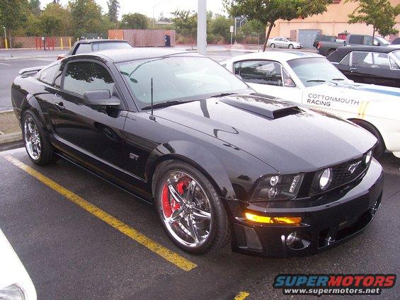 Black Ford Mustang GT with aftermarket hood scoop and chrome wheels parked in a lot