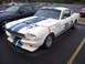2002 Ford Mustang - A classic white Shelby GT350 race car with blue racing stripes is parked in a lot next to a modern black car.