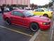 2002 Ford Mustang - A red Ford Mustang is parked in a lot, with a yellow Mustang nearby and several people milling around.