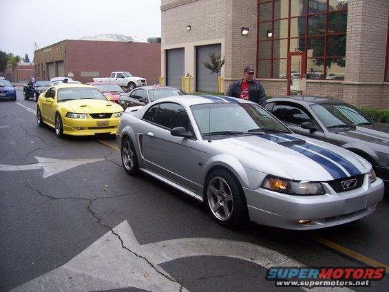 Silver 2002 Ford Mustang with blue stripes parked in a line of cars