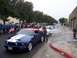 2002 Ford Mustang - A blue Ford Mustang, decorated with an American flag, is seen at a parade event alongside other vehicles and participants.