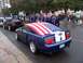 2002 Ford Mustang - A blue Ford Mustang, likely a 2005 model, is decorated with an American flag during a parade.