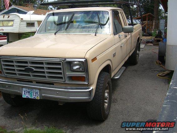Tan Ford pickup truck with a roof rack and a camper shell in the background