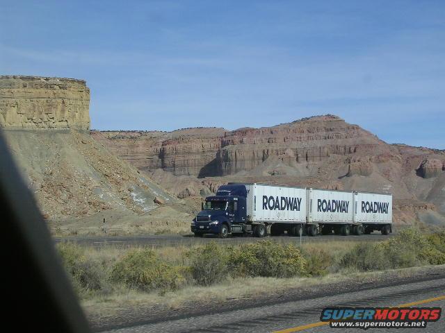 Blue semi-truck pulling two white Roadway trailers on a highway with desert mountains in the background