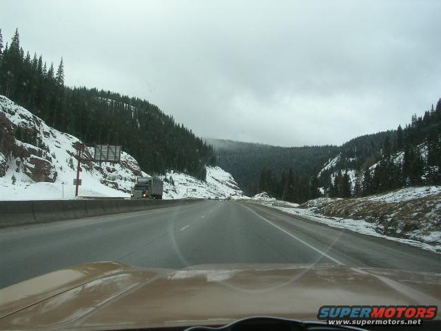 Brown car dashboard and windshield view on a snowy mountain highway with a truck ahead
