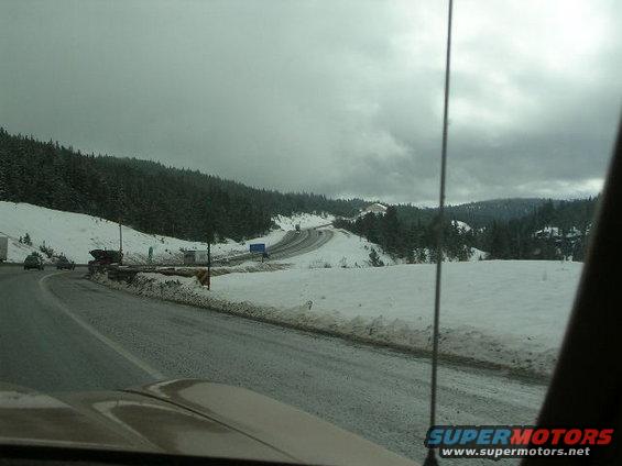 View from a car on a snowy highway with trees and other vehicles