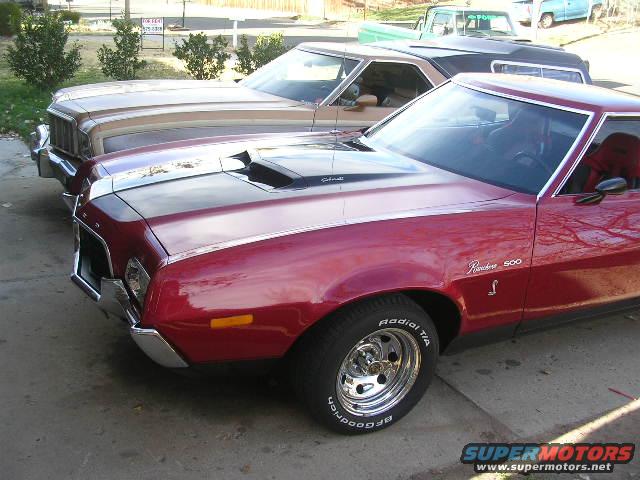 Red 1975 Ford Ranchero 500 with a black hood scoop and tan Ford LTD II parked side-by-side