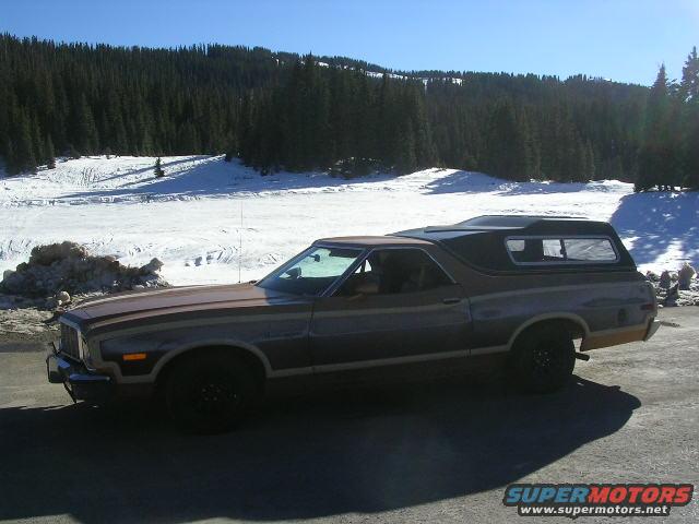 Side view of a 1975 Ford Ranchero with a camper shell in a snowy landscape
