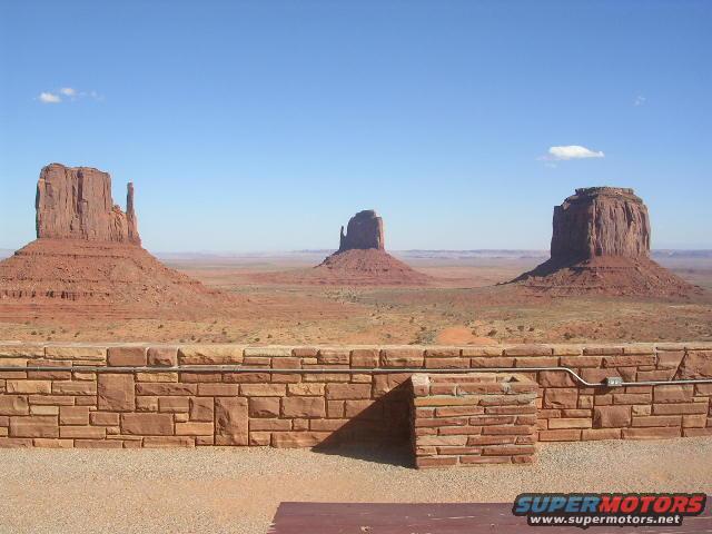 Monument Valley with mesas and buttes under a blue sky, viewed over a stone wall