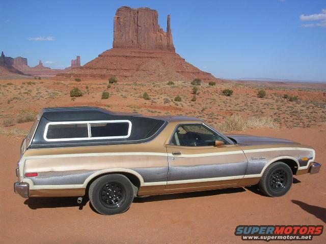 Gold and brown Ford Ranchero with black camper shell parked on dirt road, Monument Valley in background