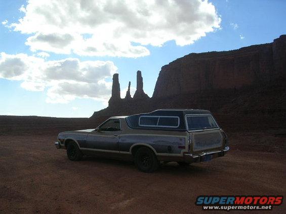 Two-tone brown and gray 1975 Ford Ranchero with camper shell parked in desert landscape