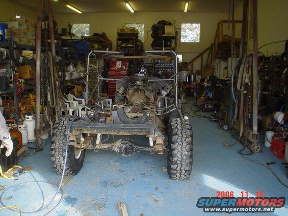 Off-road vehicle chassis in garage, undergoing assembly. Engine and drivetrain visible