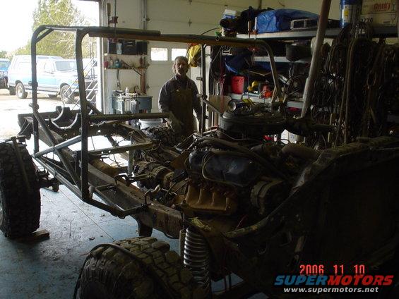 Vehicle chassis with engine and roll cage in a garage, viewed from the front