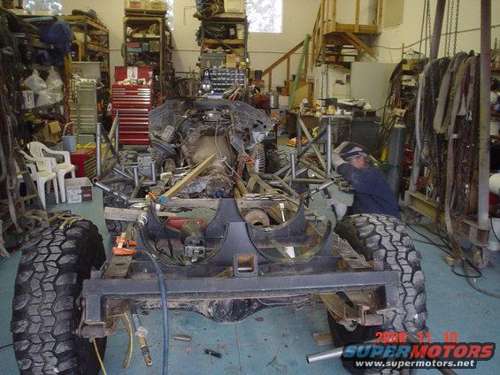 Vehicle frame with large tires and engine components, being worked on in a garage