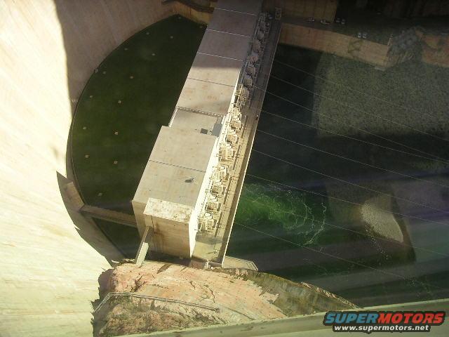View from above of a large concrete dam structure with a reservoir of green water
