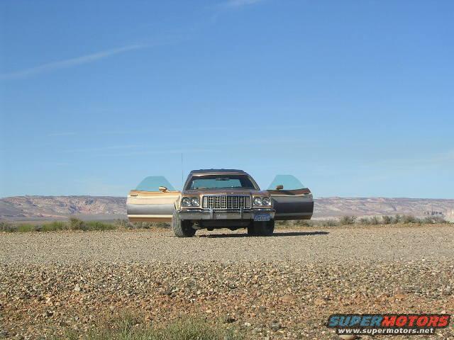 Brown 1975 Ford Ranchero with doors open, parked on gravel with desert landscape