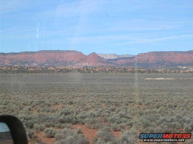 View of desert terrain and red rock mountains under a blue sky, seen from a vehicle