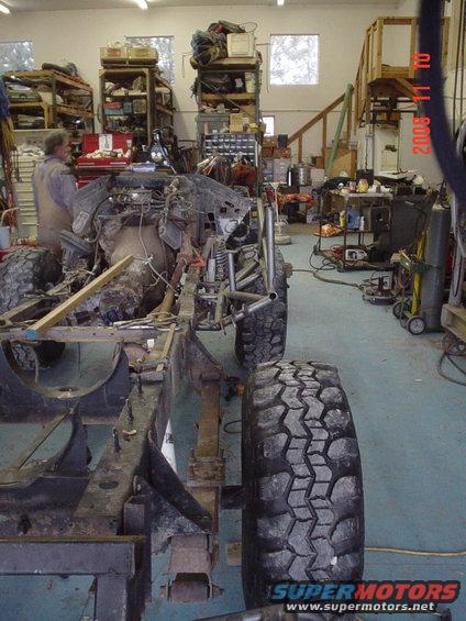 1978 Ford Bronco frame with engine and large tires in a workshop, viewed from the side