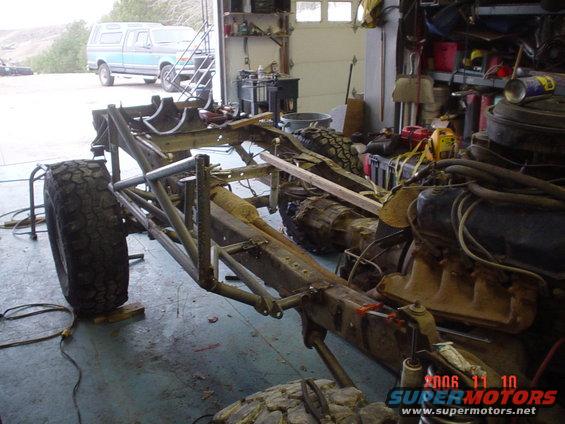 Custom off-road chassis with large tires and engine. Blue pickup truck in background