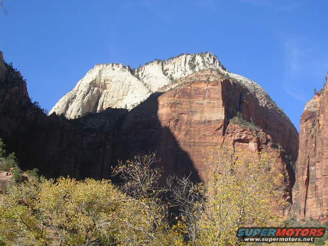 Mountain landscape with yellow trees and blue sky. Supermotors.net logo