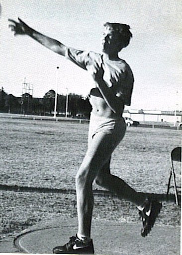Athlete in mid-throw on a track field, wearing shorts and t-shirt