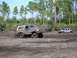 1989 Ford Bronco - A muddy 1989 Ford Bronco navigates a challenging off-road terrain, with another vehicle partially submerged in the mud behind it.