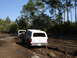 1989 Ford Bronco - Two white SUVs navigate a muddy track through a wooded area on a sunny day.