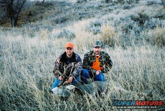 Two hunters pose with a deer in a field