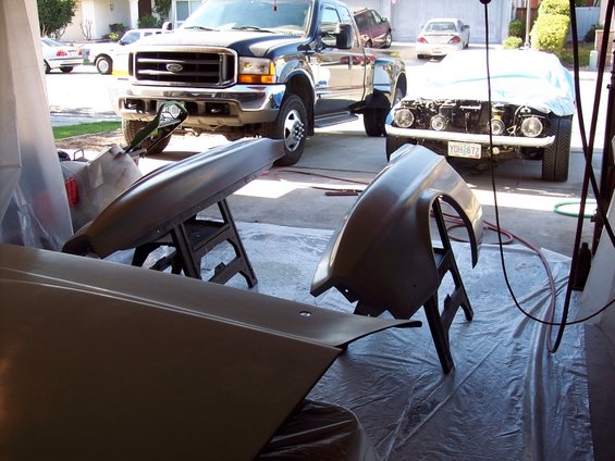 Car parts on sawhorses in front of a Ford truck and a covered car
