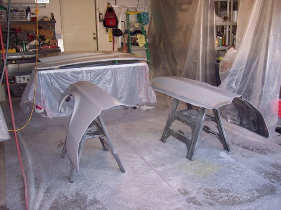 Car fender and hood on sawhorses in a garage, covered in plastic sheeting