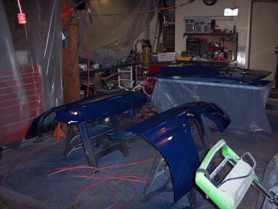 Two dark blue car fenders on sawhorses in a garage with red cords on the floor