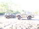 1989 Ford Bronco - Two off-road vehicles, a Ford Bronco and a Jeep Wrangler, are covered in mud after driving through a sandy, wooded area.