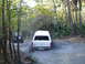 1989 Ford Bronco - A white SUV navigates a muddy path in a wooded area, with another vehicle visible ahead.