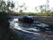 1989 Ford Bronco - A black SUV navigates a challenging muddy terrain, kicking up water and mud.
