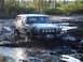 1989 Ford Bronco - White SUV navigating a muddy track, splashing through the mire.