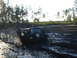 1989 Ford Bronco - Off-road Jeep Wrangler navigates a muddy track, creating a large splash.