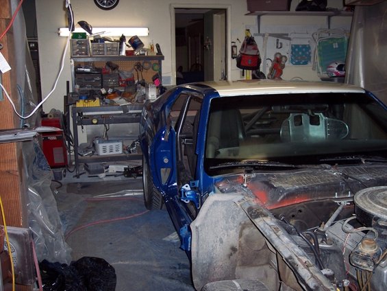 Blue and gold car in a garage, undergoing repairs. Front end is disassembled