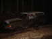 1989 Ford Bronco - A mud-covered SUV is stuck in a wooded area at night, with a driver visible inside.