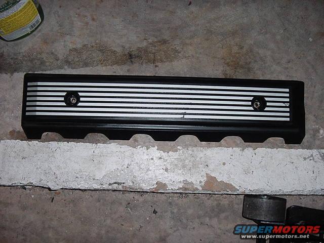 Black engine valve cover with silver horizontal stripes and two bolts