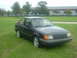 1989 Ford Escort - A dark 1989 Ford Escort coupe sits on a grassy lawn in front of a modern building.