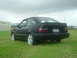1989 Ford Escort - The rear of a black 1989 Ford Escort coupe is visible, parked on a grassy field under an overcast sky.