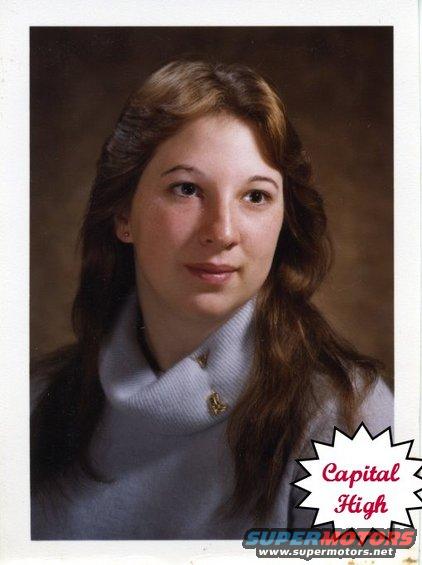 Woman in a light blue turtleneck sweater with a gold pin on the collar